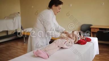 老年妇女按摩师给医院里的小女孩做腹部按摩。